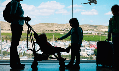 Family at airport window with pushchair and suitcase, aeroplane in sky. Travel support from a Mortgage Broker Gold Coast.