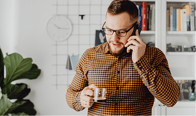 Mortgage Broker Gold Coast talking on the phone, holding a mug in a bright office with bookshelves, plant, and wall clock.