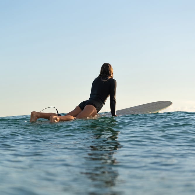A person in a black wetsuit kneels on a surfboard in calm sea waters, gazing at the horizon near the Gold Coast.