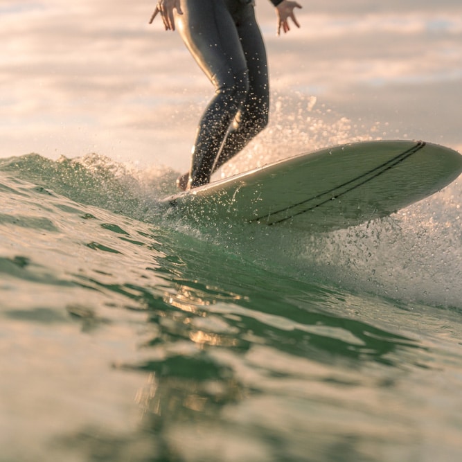 A surfer in a wetsuit rides a sunset wave near the Gold Coast, water splashing as only their legs and board are visible.
