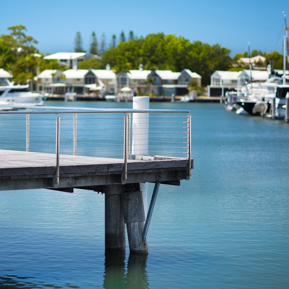 A wooden jetty over calm blue water in Coomera, with boats, modern homes, and trees—Mortgage Broker Gold Coast setting.