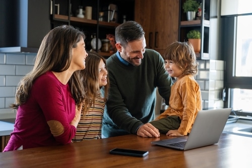 A happy family of four consults with a Mortgage Broker Gold Coast at home, laughing together around their bright kitchen worktop.