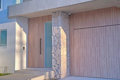 Modern house entrance with wooden panelling, stone column, frosted glass door, and garage. Mortgage Broker Gold Coast can help.